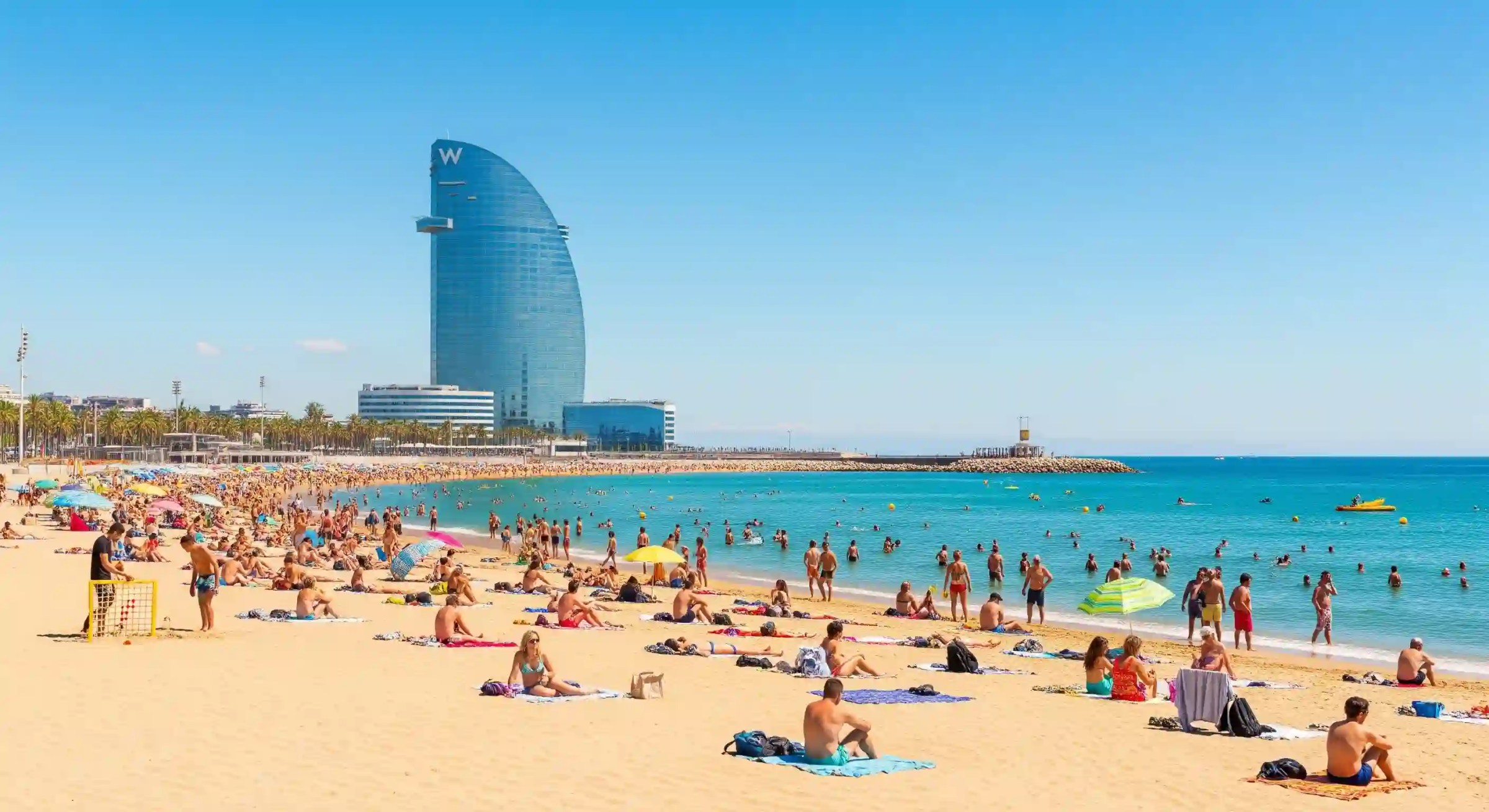 Barcelona Beaches Crowded beach of Barcelona with people sunbathing and swimming, tall modern hotel building in background.