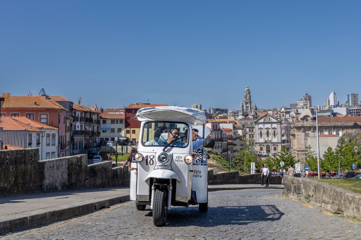 White tuk-tuk on cobblestone street, cityscape in background.
