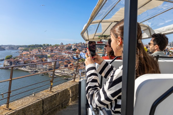 Tourists on a bus take photos of a scenic cityscape and river.