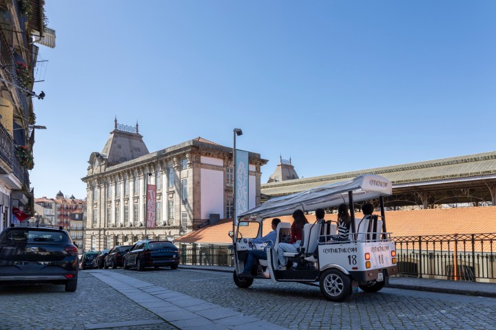 Street view with a tuk-tuk vehicle and historic buildings under clear blue sky.