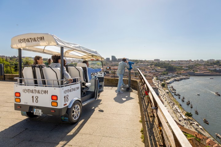 Tourists in a white open vehicle enjoy a river view from a scenic overlook.