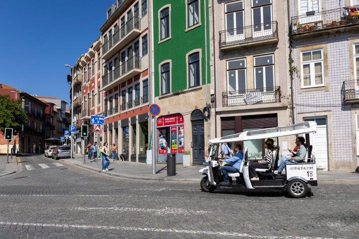 Tuk-tuk driving on a street lined with colorful historic buildings.