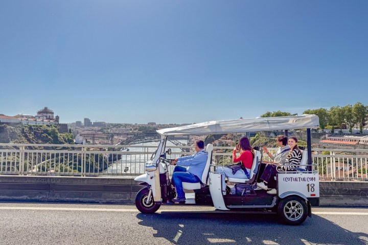 A white open-air vehicle with three passengers on a scenic road view.