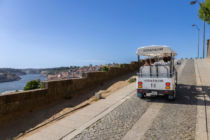 Tourist golf cart on cobblestone road with city and river view.